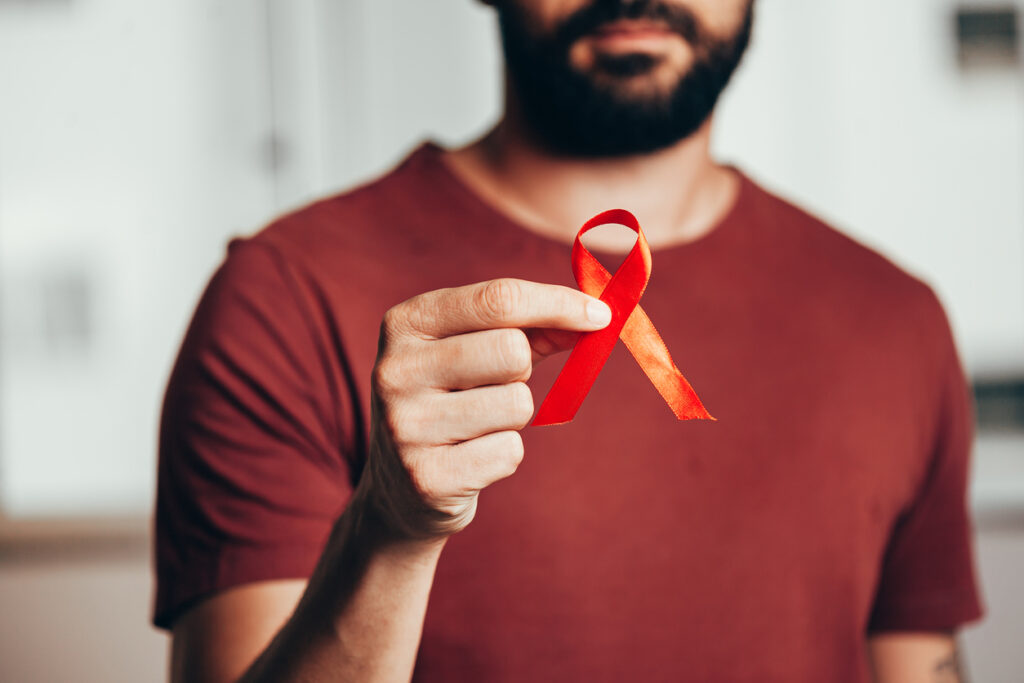 Man holds out red AIDS ribbon 