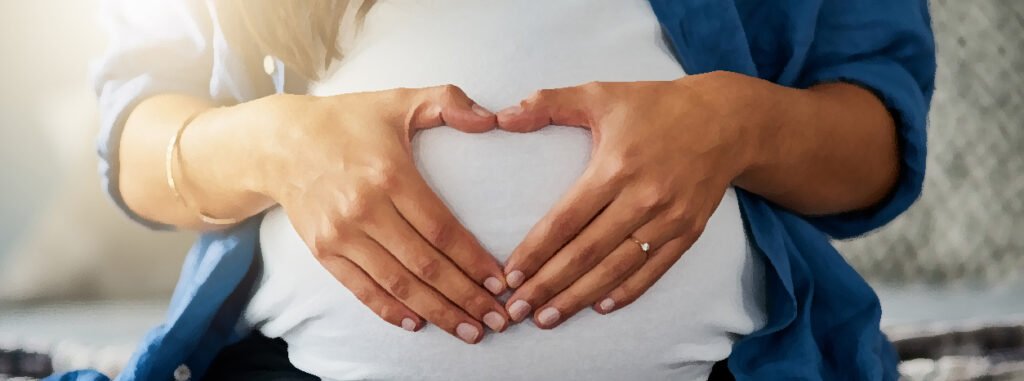 Pregnant woman making a symbol of a heart with her hands, over her stomach